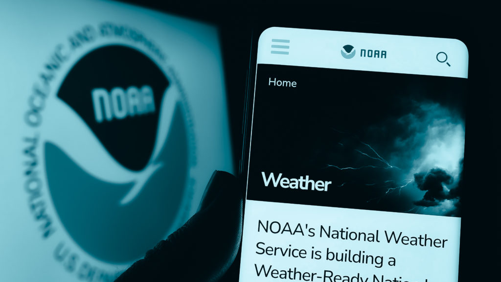 A hand holding a phone that is showing the NOAA homepage.