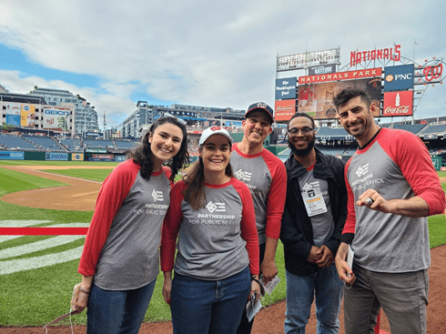 5 people wearing matching red and grey shirts at a Nationals baseball game